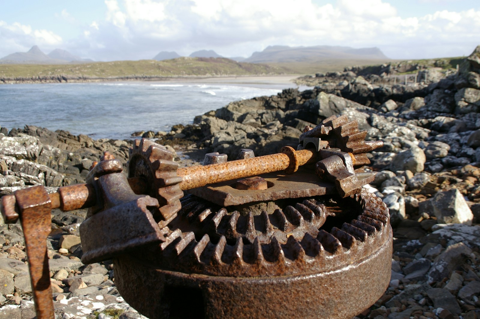 an old rusty water pump sitting on a rocky beach