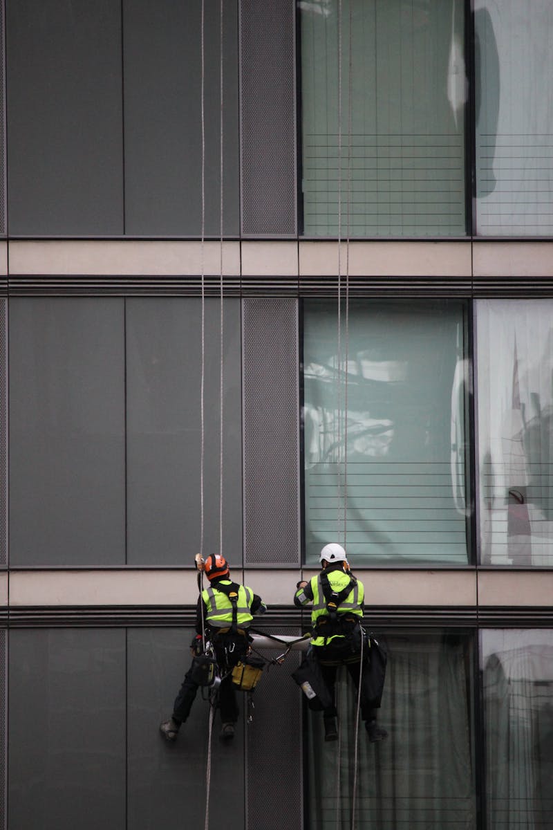 Two window cleaners suspended from ropes work on glass facade of a high-rise building.